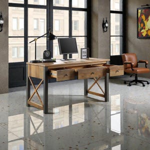 May include: A wooden desk with two open drawers, a computer monitor, and a black desk lamp. The desk has a light brown wooden top and gray metal legs. A brown leather office chair is in the background.