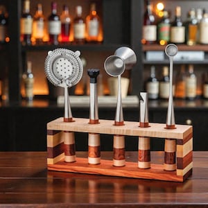 May include: A set of stainless steel bar tools, including a strainer, muddler, jiggers, bottle opener, and spoon, displayed in a wooden holder. The holder is made of light and dark wood, with a natural finish. The bar tools are designed for mixing cocktails.