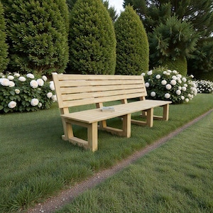 Puede incluir: Un banco de parque de madera clara con respaldo de listones y asiento rectangular. El banco está sobre un césped, rodeado de arbustos verdes y flores blancas. Un pequeño libro descansa sobre el asiento.