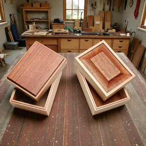 Pode incluir: Quatro caixas de madeira com tampas, exibidas em uma mesa de madeira. As caixas têm uma moldura de cor clara e uma parte superior marrom avermelhada mais escura. O interior das caixas também é de madeira mais escura. As caixas estão abertas.