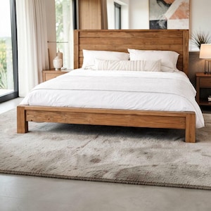 May include: A wooden bed frame with a matching headboard. The bed is covered with white bedding and pillows. The room has a neutral color palette with a light gray rug and a large window.