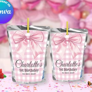 Könnte beinhalten: Zwei silberne Beutel mit rosa-weißem Karomuster und rosa Schleifen. Die Beutel haben Etiketten mit der Aufschrift "Charlotte's 1st Birthday 03 NOV 2024".