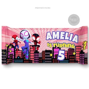 Puede incluir: Envoltorio rosa para barra de caramelo con personajes de superhéroes y un paisaje urbano. El texto "AMELIA IS TURNING 5" es visible. El envoltorio tiene un diseño de cómic.