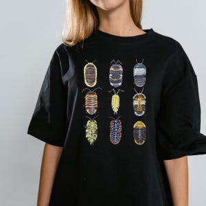 Puede incluir: Camiseta negra con un estampado gráfico de cochinillas de diferentes colores.