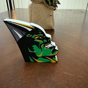 May include: A green and black 3D foam cutout of a cartoon monster with a toothy grin. The monster is facing right and has a white background.