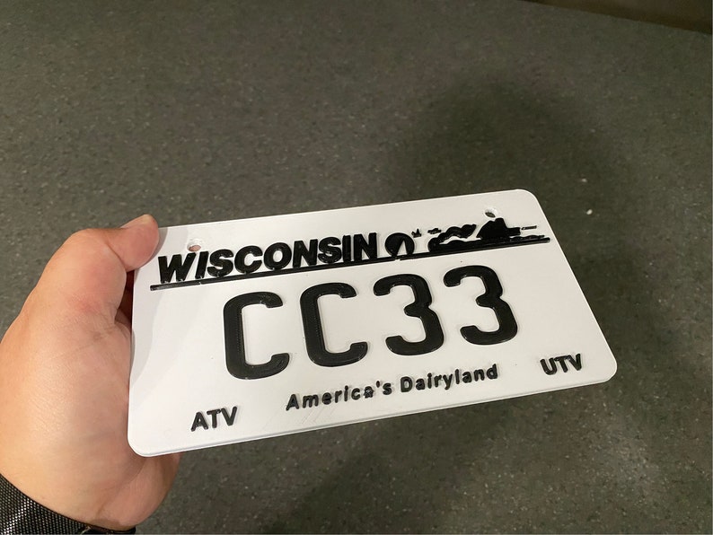 May include: White Wisconsin license plate with black text and a black silhouette of a vehicle. The plate number is CC33. The text on the plate reads "Wisconsin" and "America's Dairyland". The plate also has the abbreviations "ATV" and "UTV" on the bottom.