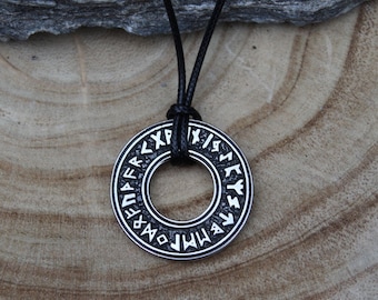 May include: A silver pendant necklace with a circular pendant featuring a circle of Norse runes. The pendant is on a black cord.
