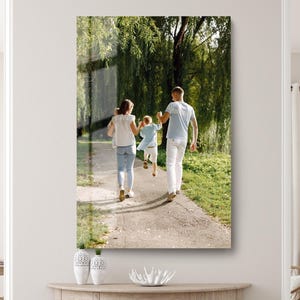 May include: A framed print of a family walking on a path in a park. The family consists of two adults and two children. The adults are wearing white shirts and jeans. The children are wearing light blue shirts and shorts. The background is a green park with trees.