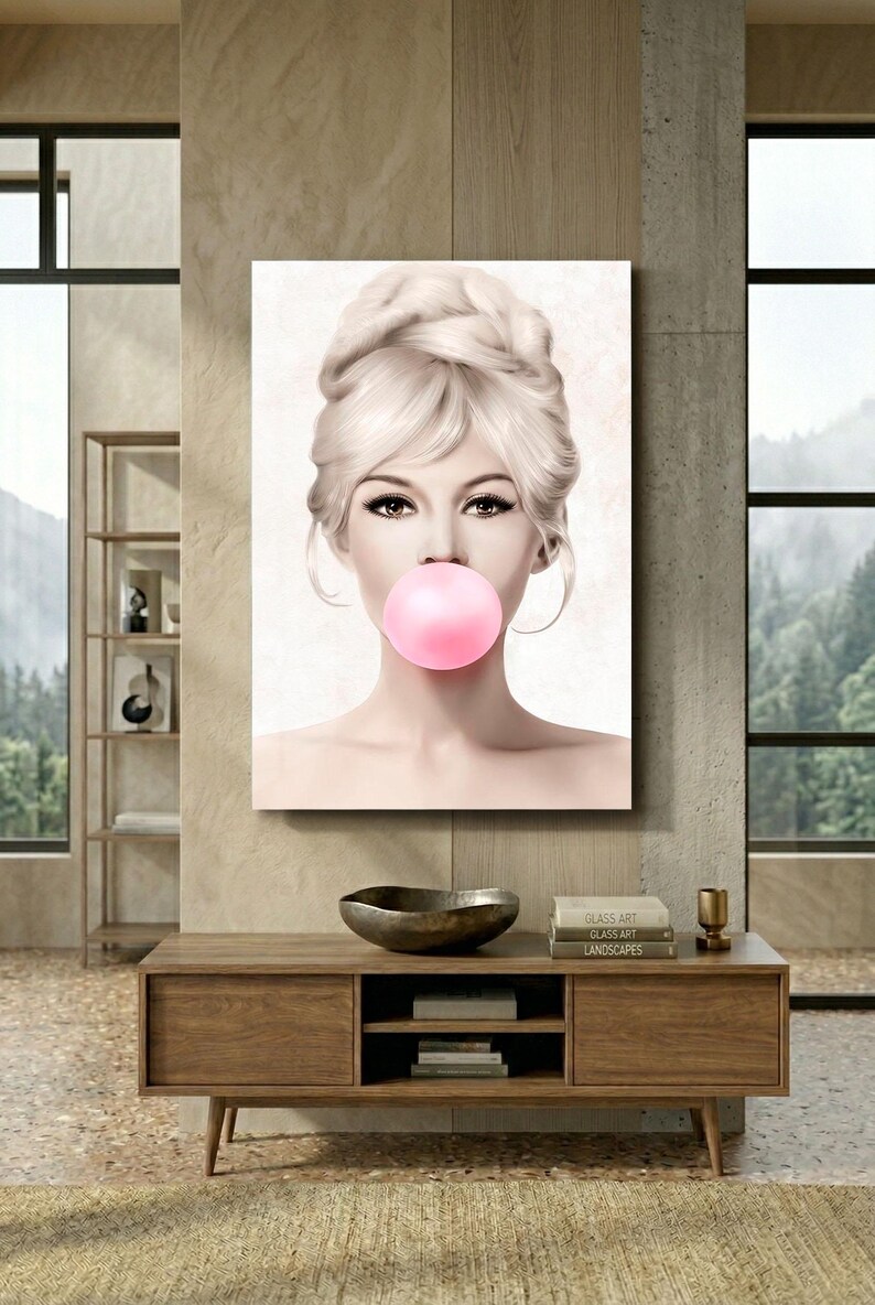 May include: A canvas print featuring a portrait of a woman with blonde hair styled in an updo, blowing a large pink bubblegum bubble. The artwork is displayed on a wall above a wooden cabinet, creating a stylish interior design.
