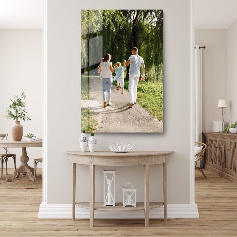 May include: A framed print of a family walking on a path in a park. The family consists of two adults and two children. The adults are wearing white shirts and jeans. The children are wearing light blue shirts and shorts. The background is a green park with trees.