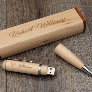 Puede incluir: Un bolígrafo de madera y una caja de madera a juego con el nombre "Robert Williams" grabado en ella. El bolígrafo tiene una unidad USB en un extremo.