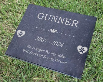 May include: Black granite pet memorial stone with the name "Gunner" engraved, dates "2005 - 2024", and the text "No Longer By My Side But Forever In My Heart". Two paw print hearts are engraved on the stone.