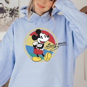 Puede incluir: Una sudadera con capucha azul claro con un gr&aacute;fico vintage de Mickey Mouse y el texto "Mickey Mouse" en una fuente manuscrita.