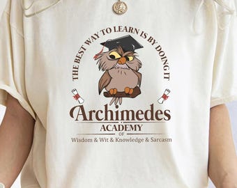 May include: A white t-shirt with a brown owl wearing a graduation cap. The text on the shirt reads "THE BEST WAY TO LEARN IS BY DOING IT" and "Archimedes ACADEMY OF Wisdom & Wit & Knowledge & Sarcasm".