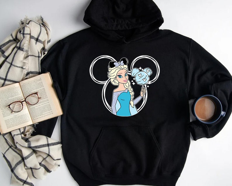 Puede incluir: Sudadera con capucha negra con una silueta blanca de Mickey Mouse que presenta una imagen de dibujos animados de Elsa de Frozen sosteniendo un algod&oacute;n de az&uacute;car azul y blanco.