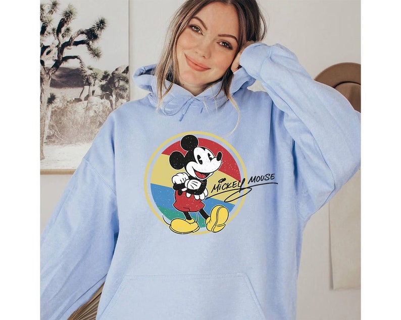 Puede incluir: Una sudadera con capucha azul claro con un gr&aacute;fico vintage de Mickey Mouse y el texto "Mickey Mouse" en una fuente manuscrita.