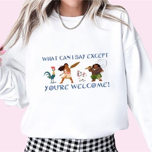 May include: White sweatshirt with a graphic print of characters from the animated movie Moana. The text on the shirt reads "What can I say except you're welcome!"