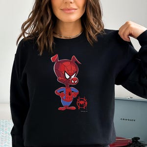 Puede incluir: Sudadera negra con un cerdo de dibujos animados que lleva un traje de Spider-Man rojo y azul. El cerdo est&aacute; de pie con los brazos cruzados y tiene una expresi&oacute;n seria. Hay un peque&ntilde;o s&iacute;mbolo de Spider-Man debajo del cerdo.