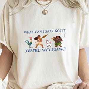 May include: A white t-shirt with a blue graphic print featuring characters from the animated movie Moana. The text on the shirt reads "What can I say except you're welcome!"