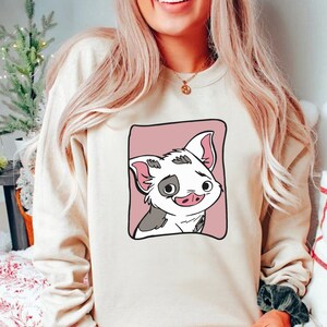 May include: A cream-colored sweatshirt with a cartoon pig illustration. The pig is white with black spots and has a pink nose and ears. The pig is surrounded by a pink square.