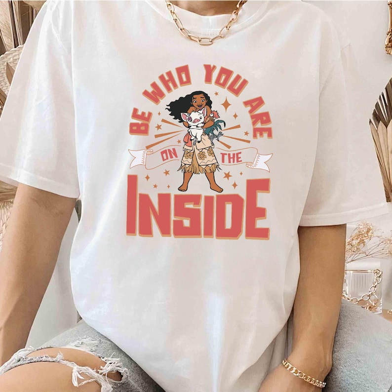 May include: White t-shirt with a pink and orange graphic design featuring a cartoon character with a pig. The text on the graphic says "Be who you are on the inside".