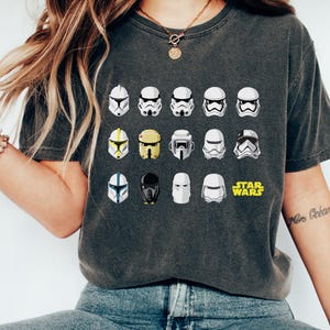 May include: A dark gray t-shirt with a graphic of various Star Wars Stormtrooper helmets. The text "STAR WARS" is printed in yellow below the helmets.