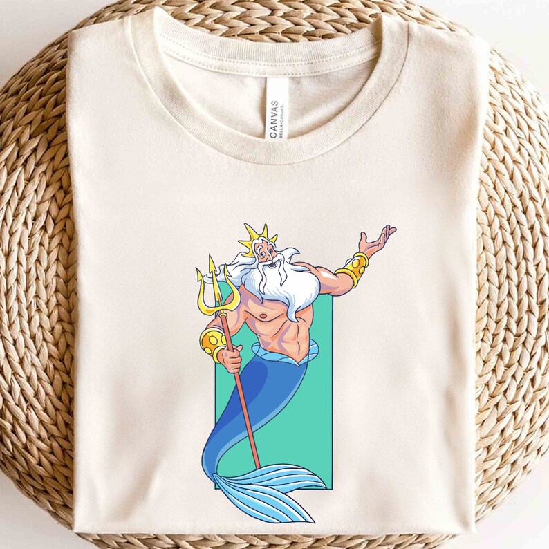 K&ouml;nnte beinhalten: Ein wei&szlig;es T-Shirt mit einem Cartoon-Bild von K&ouml;nig Triton aus Disneys Arielle, die Meerjungfrau. Er h&auml;lt seinen Dreizack und hat eine goldene Krone und einen Bart. Der Hintergrund ist hellgr&uuml;n.