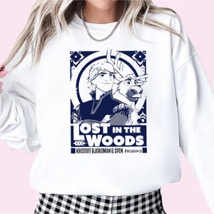 Puede incluir: Sudadera blanca con un gr&aacute;fico azul de Kristoff y Sven de Frozen II. El gr&aacute;fico dice "Lost in the Woods" y "Kristoff Bjorgman & Sven Frozen II".