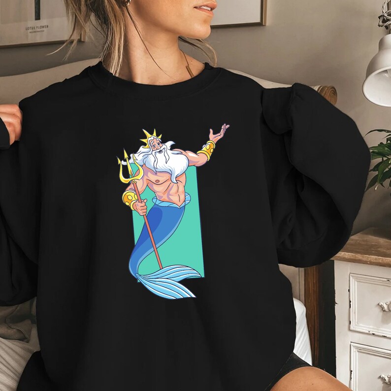 K&ouml;nnte beinhalten: Schwarzes Sweatshirt mit einem Aufdruck von K&ouml;nig Triton aus Arielle, die Meerjungfrau. Er h&auml;lt einen Dreizack und tr&auml;gt eine Krone.