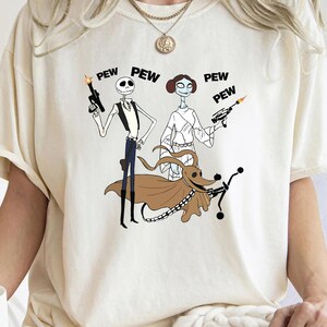 May include: White t-shirt with a graphic print of characters from the Nightmare Before Christmas and Star Wars. The characters are dressed as Han Solo, Princess Leia, and a dog. The text "PEW PEW PEW" is printed above the characters.