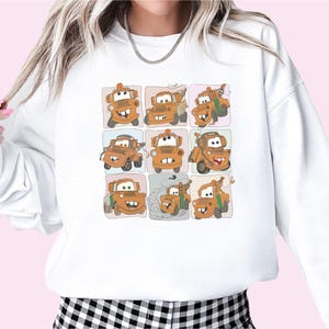 Puede incluir: Sudadera blanca con una imagen de dibujos animados de una gr&uacute;a de remolque con diferentes expresiones faciales en un patr&oacute;n de cuadr&iacute;cula.