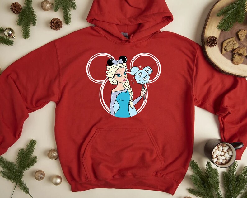 Puede incluir: Sudadera roja con capucha con un contorno blanco de las orejas de Mickey Mouse. Dentro de las orejas hay una imagen de dibujos animados de Elsa de Frozen sosteniendo un algod&oacute;n de az&uacute;car azul.