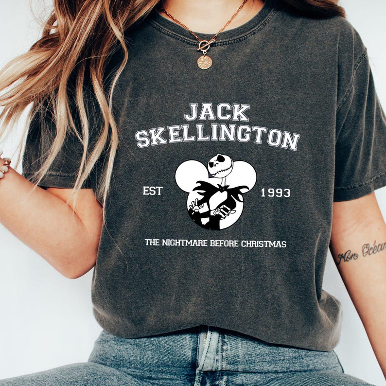May include: A black t-shirt with a white graphic of Jack Skellington from "The Nightmare Before Christmas" in a Mickey Mouse silhouette. The text "Jack Skellington" is above the graphic, and "EST 1993" is below the graphic.