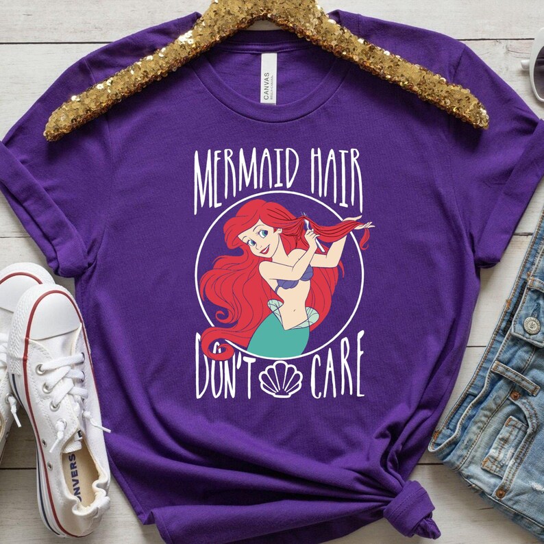 May include: Purple t-shirt with a white graphic of Ariel from The Little Mermaid. The graphic says "Mermaid Hair Don't Care" and features a seashell.