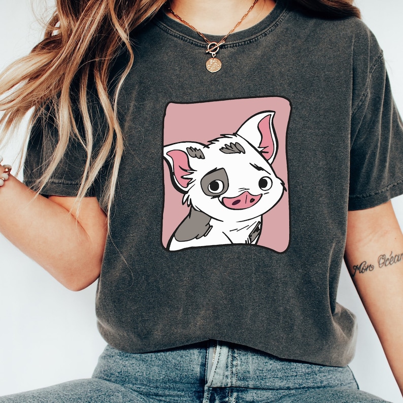 May include: A dark gray t-shirt with a pink square graphic of a cartoon pig with black and white spots. The pig has a pink nose and is looking to the right.