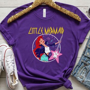 May include: Purple t-shirt with a graphic of Ariel from The Little Mermaid playing an electric guitar. The text "Little Mermaid" is above the graphic.