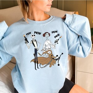 May include: Light blue sweatshirt with a graphic print of Jack Skellington and Sally from The Nightmare Before Christmas dressed as Star Wars characters. The text "PEW PEW PEW" is printed above the characters.