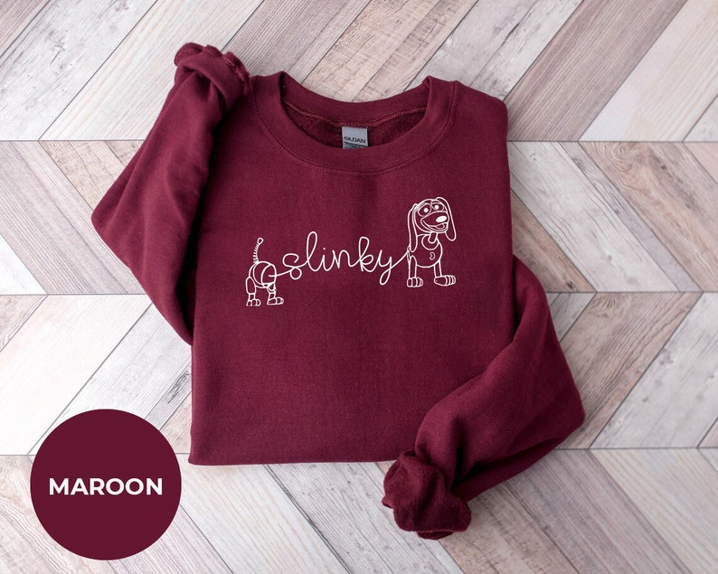 May include: Maroon sweatshirt with a white outline of Slinky Dog from Toy Story. The text "Slinky" is written in cursive.