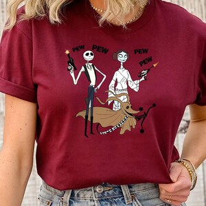 May include: Red t-shirt with a graphic print of Jack Skellington, Sally, and Zero from Nightmare Before Christmas dressed as Star Wars characters. The text "PEW PEW" is printed on the shirt.