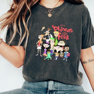 May include: A dark gray t-shirt with a vintage-style graphic of the characters from the Disney cartoon "Phineas and Ferb".