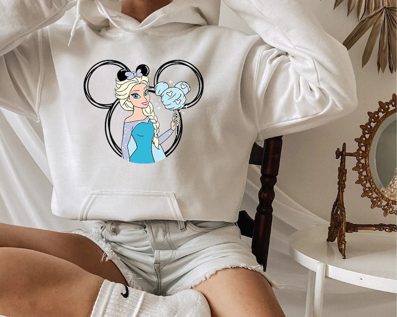 Puede incluir: Sudadera con capucha blanca con un gr&aacute;fico en blanco y negro de una princesa Disney de dibujos animados sosteniendo una piruleta azul y blanca. La princesa lleva un vestido azul y tiene el pelo rubio.
