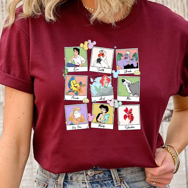 May include: Burgundy t-shirt with a grid of nine framed images of characters from The Little Mermaid. Characters include Eric, Scuttle, Ursula, Flounder, Ariel, Max, King Triton, Melody, and Sebastian. Each image has a Mickey Mouse-shaped accent.