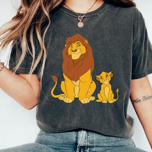 May include: A dark gray t-shirt with a cartoon image of Simba and Mufasa from The Lion King. The shirt features a brown mane and yellow fur on the lions.