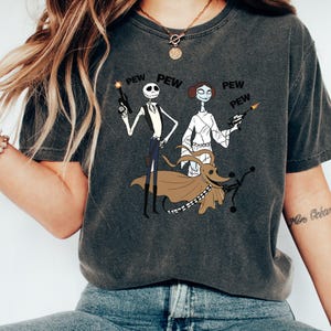 May include: A dark gray t-shirt with a graphic print of Jack Skellington and Sally from The Nightmare Before Christmas dressed as Han Solo and Princess Leia from Star Wars. The text "PEW" appears multiple times on the shirt.