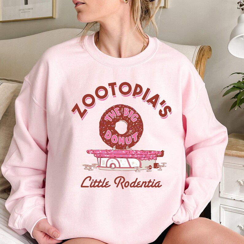 May include: Pink sweatshirt with a graphic of a donut shop called "Zootopia's The Big Donut" with the text "Little Rodentia" below the graphic.