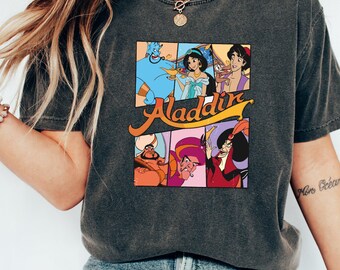 May include: A dark gray t-shirt with a vintage-style graphic of characters from the Disney movie Aladdin. The graphic features Aladdin, Jasmine, Genie, Abu, Jafar, and Rajah. The text "Aladdin" is written in a retro font.
