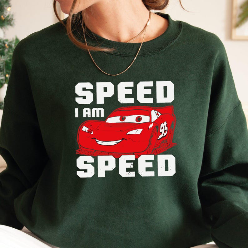 Puede incluir: Sudadera verde con un coche de carreras rojo de dibujos animados y el texto "SPEED I AM SPEED" en blanco.