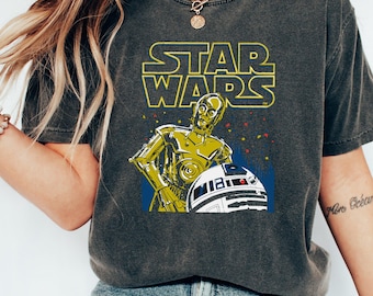 以下が含まれることがあります： C-3POとR2-D2が描かれたビンテージスタイルのスターウォーズのグラフィックがプリントされたダークグレーのTシャツ。キャラクターの上に「STAR WARS」という文字が黄色でプリントされています。