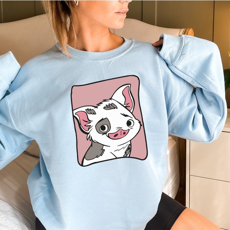 May include: A light blue sweatshirt with a cartoon pig illustration on the front. The pig is white with black spots and has a pink nose and ears. The pig is surrounded by a pink rectangle.