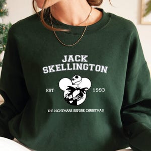 May include: Green sweatshirt with a white graphic of Jack Skellington from The Nightmare Before Christmas. The graphic includes the text "Jack Skellington", "Est. 1993", and "The Nightmare Before Christmas".